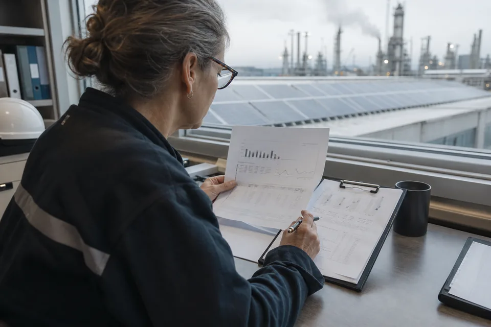 A sustainability manager checking emissions data sheets beside a plant with solar panels