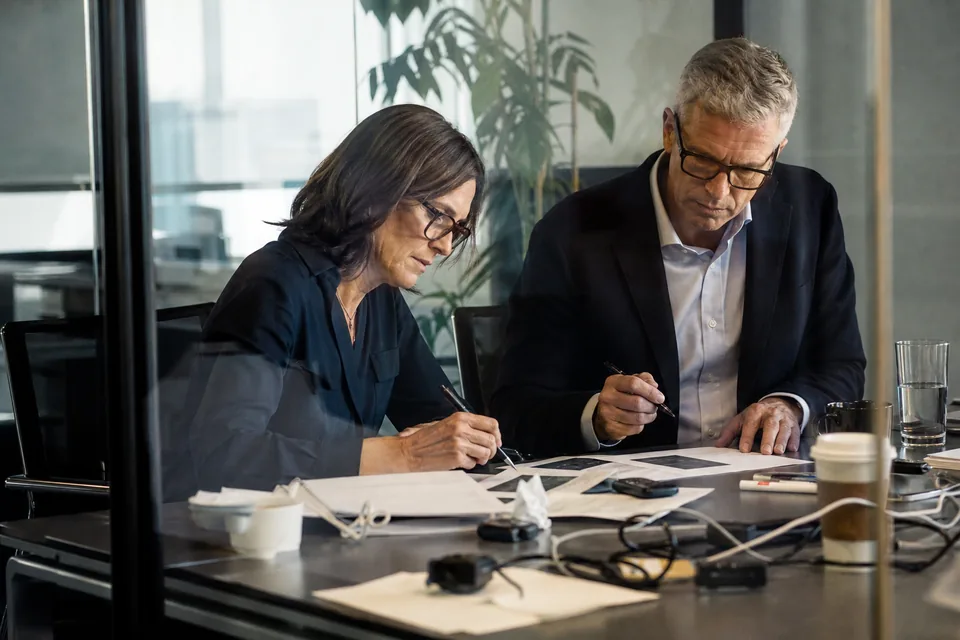 Chief financial officer and finance lead reviewing a private placement timeline on a large screen in a meeting room