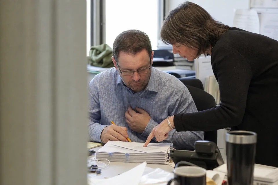 Controller and company secretary checking a quarterly report timeline on a large monitor in a finance office